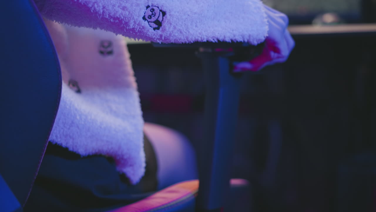 Close up of woman adjusting lever on gaming chair with hand wearing fluffy sweater under neon purple and pink lights in studio showcasing ergonomic comfort and cozy modern design mood