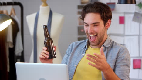 Propietario-Masculino-De-Un-Negocio-De-Moda-Con-Una-Botella-De-Cerveza-Escuchando-Música-En-Una-Computadora-Portátil-En-El-Estudio