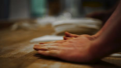 close-up shallow focus shot of baker shaping triangle slab of dough into a croissant by rolling it tightly with both hands over wooden table