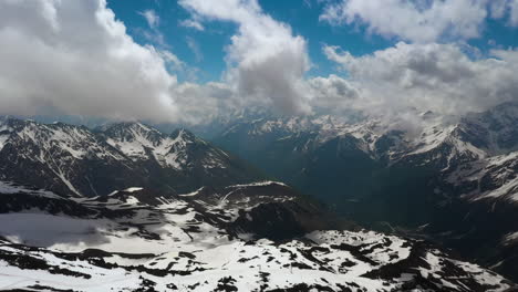 Air-flight-through-mountain-clouds-over-beautiful-snow-capped-peaks-of-mountains-and-glaciers.