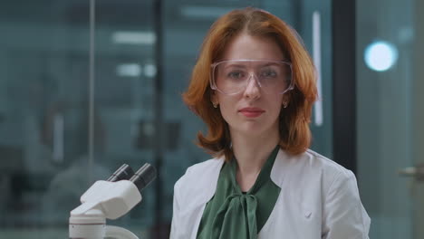 laboratorio médico en el hospital covid mujer adulta profesional de la salud está mirando en el microscopio luego subiendo la cabeza a la cámara retrato del técnico de laboratorio