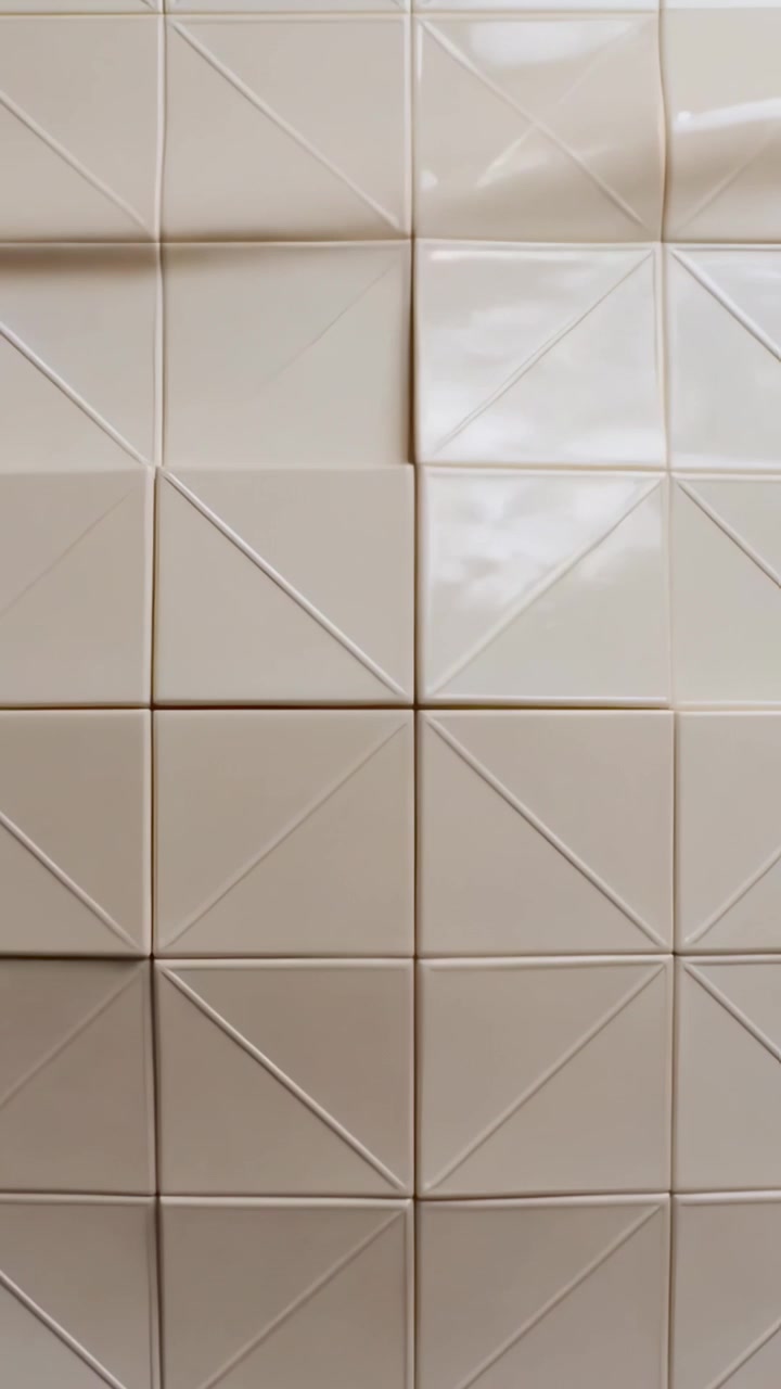 Applying glossy vinyl sheet over cream-beige tiled panel on interior wall, with light reflections
