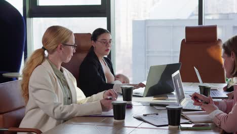 a collection of girls in business clothes of office workers while one of them breastfeeds her small child while sitting at a wooden table in a modern office