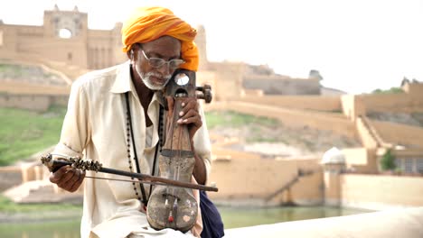 an old traditional man playing sarangi against the historic fort.