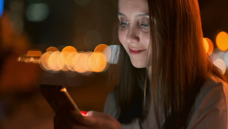 young woman tourist travels through the night megalopolis and writes text messages on social networks about the journey holds the phone in her hands and looks at the screen of the gadget