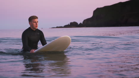 Hombre-Vestido-Con-Traje-De-Neopreno-Sentado-Y-Flotando-Sobre-Una-Tabla-De-Surf-En-Un-Mar-En-Calma