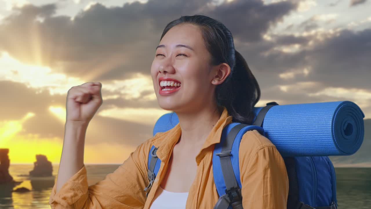 夕焼け時にビーチに立ち、成功を祝って叫び、目標を達成したことを喜ぶ登山用バックパックを背負ったアジア人女性ハイカーのクローズアップサイドビュー