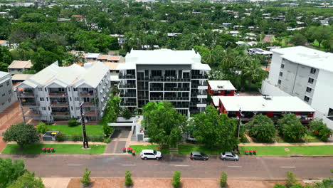 Aerial-Drone-of-Small-Modern-Styled-Apartment-Complex-By-Tropical-Houses-and-Buildings-Along-Quiet-Road-in-Australia