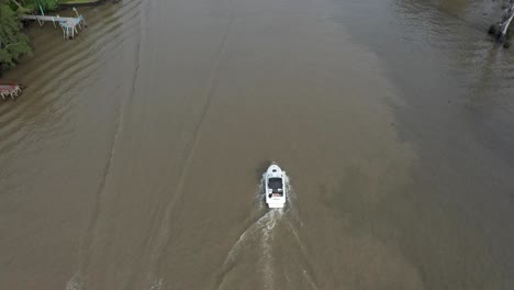 Drone-Siguiendo-Un-Bote-Motorizado-Cruzando-Un-Jet-Ski-En-Un-Río-De-Agua-Marrón-Sucia