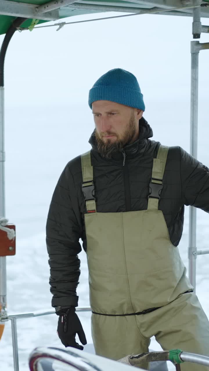 Mand i vintertøj står på en båd på havet