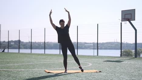 a person is engaged in performing yoga or dance on a mat set outside right next to water and a a person is engaged in performing yoga or dance on a mat set outside right next to water and a basketball court