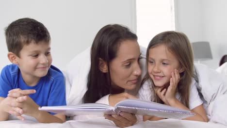 mother with her children reading story book in bedroom at home 4k