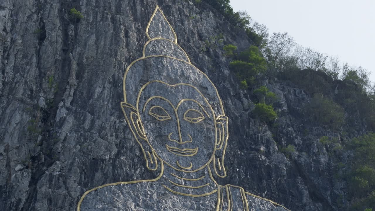 Buddha's Face engraved with gold into the hill in Khao Chi Chan, Thailand. Cinematic footage of Buddha Mountain in Pattaya at dawn. Pan forward to Buddha's golden eyes