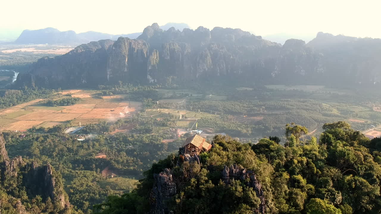 Piccola capanna di bambù in cima a una montagna durante il tramonto in Laos, con una vista mozzafiato su un paesaggio verde e sabbioso