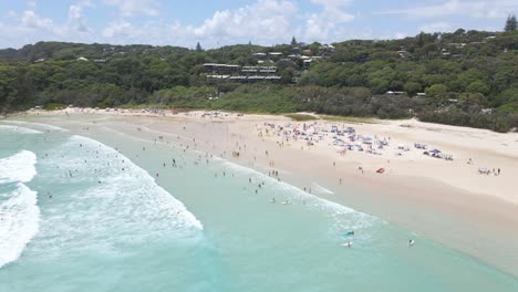 people swim and surf at cylinder beach - campground tents at sandy shore - point lookout, qld, australia