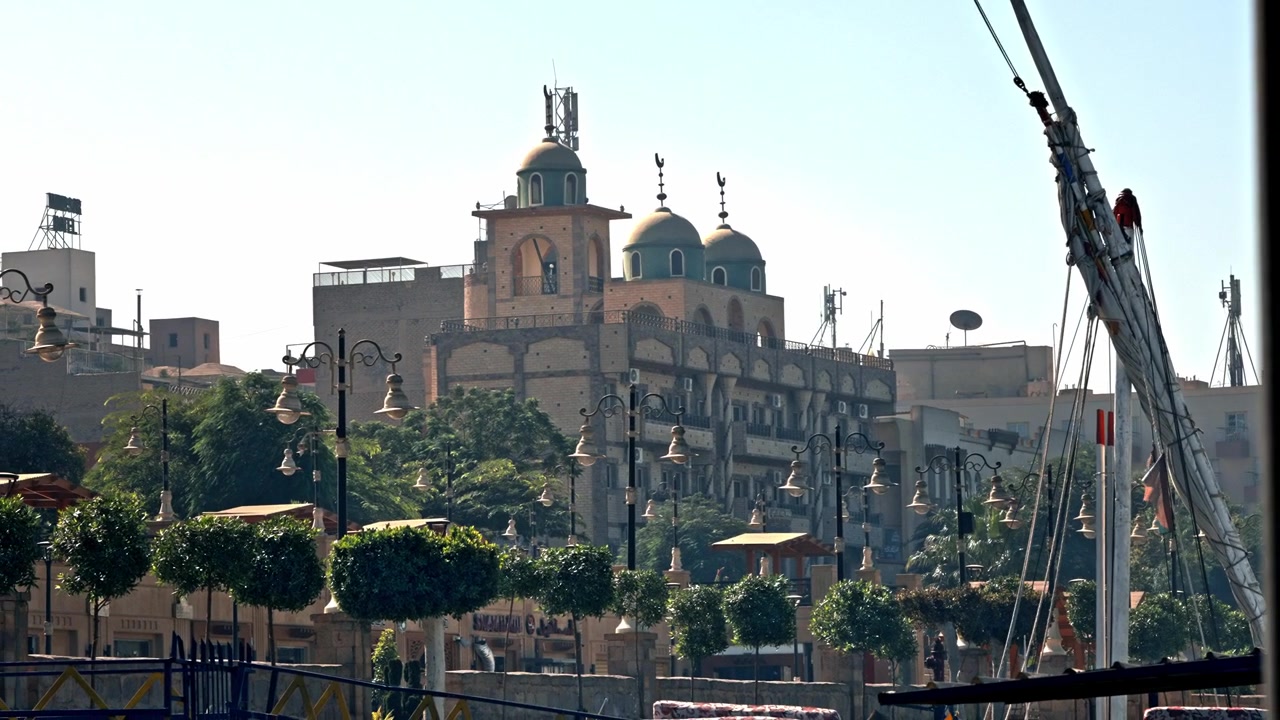 Una vista diurna della Cattedrale Copta Ortodossa della Vergine Maria (Chiesa di Santa Maria) che si erge sopra la passeggiata alberata della Corniche del Nilo a Luxor, Egitto, mostrando le sue caratteristiche cupole blu