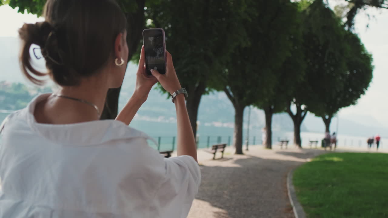 Mulher Tirando Fotos com Smartphone em um Parque Cênico à Beira do Lago