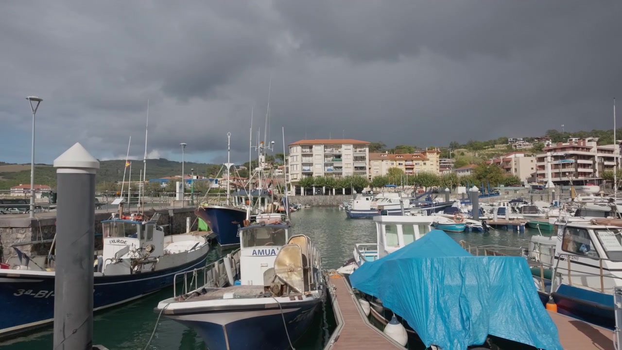 Porto di Plentzia Gorliz con molte barche ormeggiate lungo le banchine, una città costiera con edifici sulle colline sotto un cielo nuvoloso