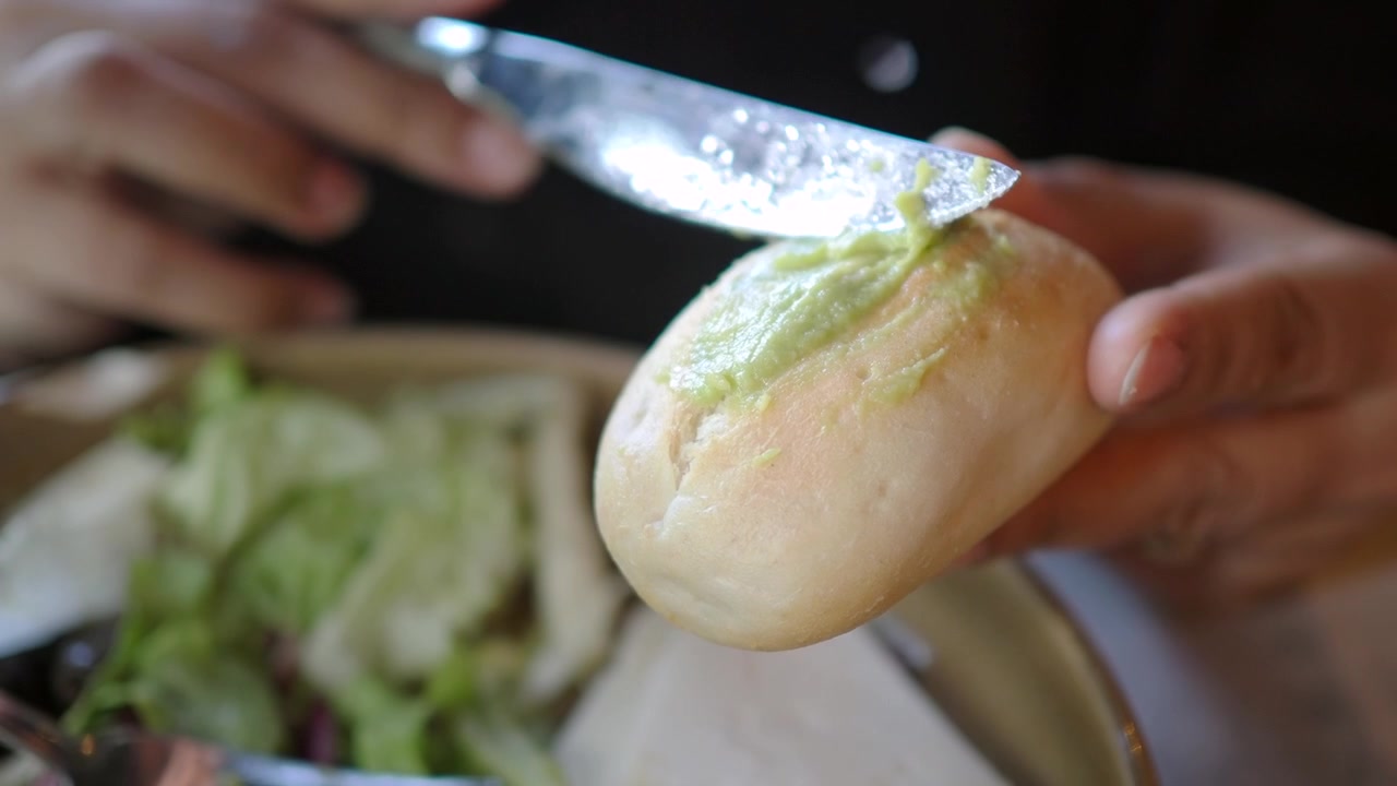 Spreading Avocado Paste on a Fresh Bread Roll