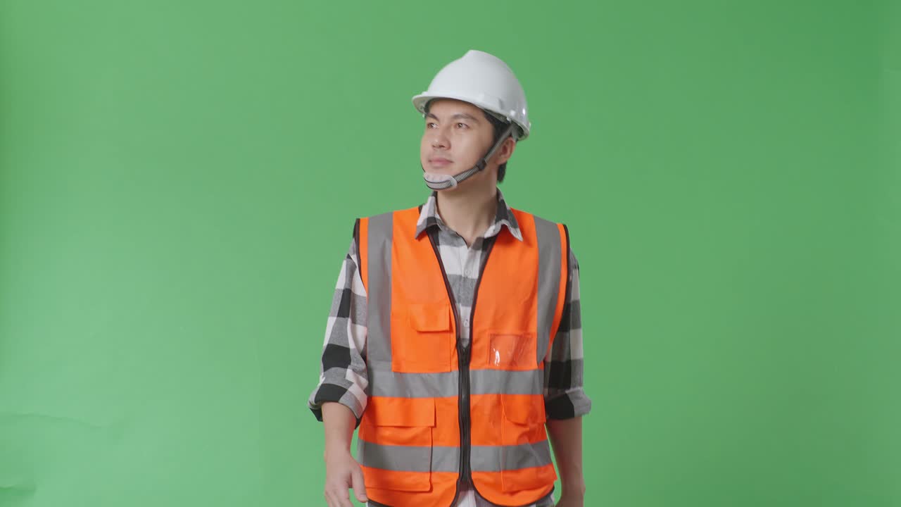 안전 헬을 입은 아시아 남성 엔지니어가 녹색 스크린 배경 스튜디오에서 는 동안 주위를 둘러보고 있습니다.