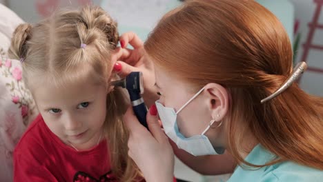 a pediatrician in a hospital checks the ear of a little girl.