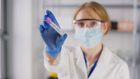 female lab research worker wearing safety glasses and mask holding test tube with pcr swab