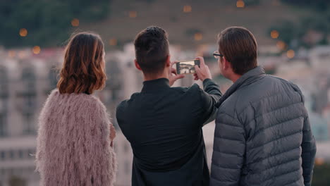 friends hanging out enjoying rooftop at sunset young man using smartphone photographing beauitful city sharing urban lifestyle on social media
