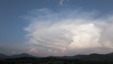 spectacular lateral drone filming of a large cumulonimbus cloud created behind a line of mountains and with a blue sky background, it evolves and we appreciate its great width,