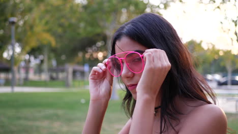 a young hispanic woman hipster wearing vintage fashion clothing and retro pink aviator sunglasses in a park playground slow motion