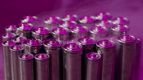 silver batteries aa and aaa in neon light with smoking fog smoke close-up. double-a battery is a standard size single cell cylindrical dry battery. batteries are common in portable electronic devices. an aa battery is composed of a single electrochemical cell that may be either a primary battery or