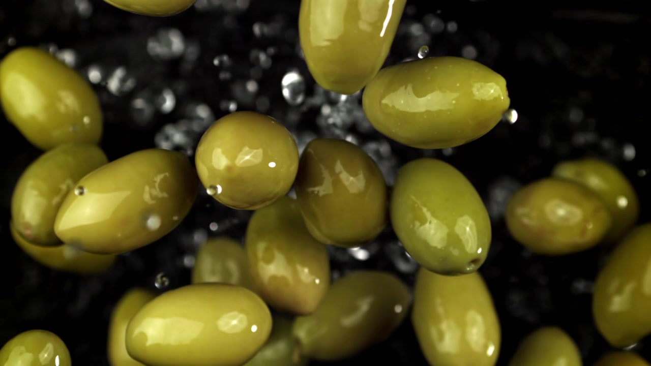 Olive verdi che cadono in super slow motion con schizzi d'acqua.