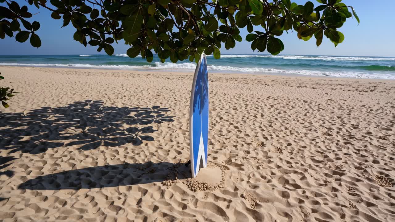 Blue surfboard standing on a tropical beach, with a tree casting a gentle shadow on the warm sand, creating a serene and tranquil atmosphere perfect for relaxation and surfing adventures