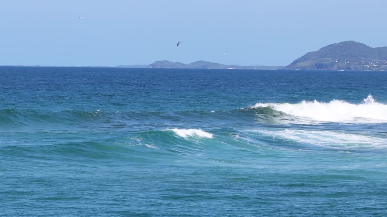Gentle ocean waves approach small islands under a clear blue sky, creating a serene marine scene.