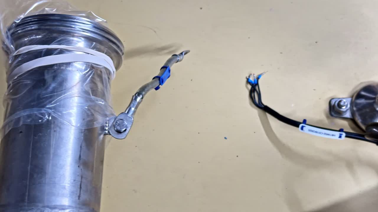 Alloggiamento cilindrico per sensore in alluminio e acciaio inossidabile avvolto in pellicola di plastica con cavo della sonda di temperatura collegato, fascette blu e terminali crimpati in un ambiente di assemblaggio industriale.