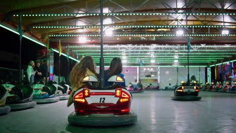 girls riding bumper car at illuminated amusement park. excited friends enjoying