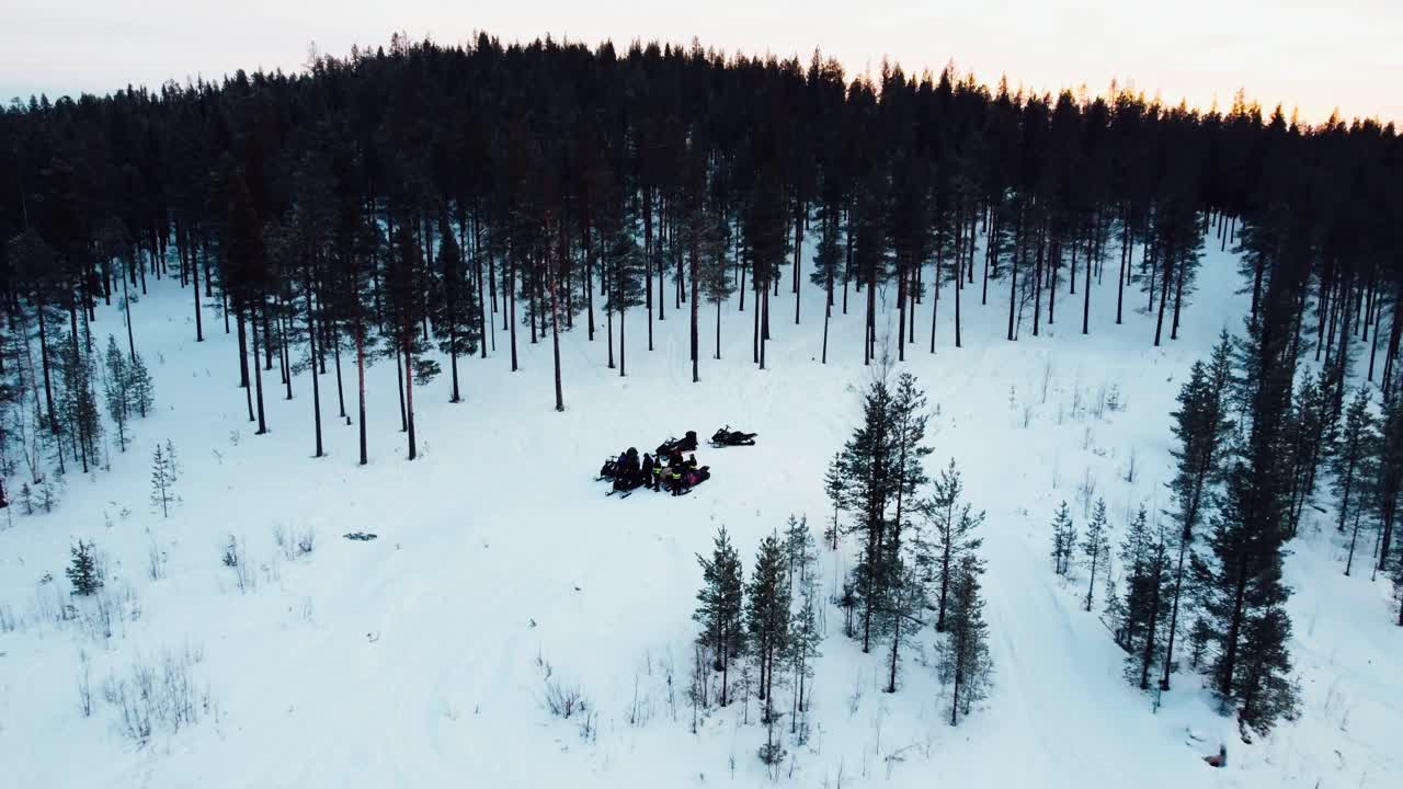 toma de drone de un grupo de personas paradas en la cima de una montaña con motos de nieve durante la puesta de sol.