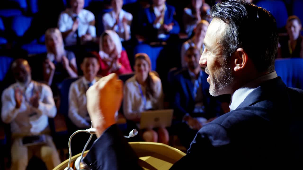 Imprenditore caucasico che parla sul palco a un seminario aziendale in auditorium 4K