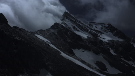 nighttime mountain peak with clouds and snow