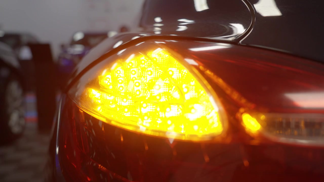 Gros plan sur le feu arrière illuminé d'une voiture de sport de luxe rouge, clignotant deux fois en rouge-orange.