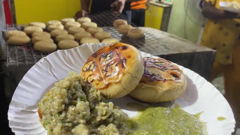 en el fondo, se ve a un vendedor horneando litti en una parrilla de hierro caliente sobre carbón y vendiendo litti chokha que se sirve con baigan bharta y chutney verde en kolkata