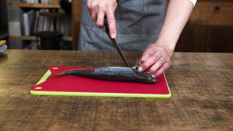 asian chef skilfully cuts off mackerel fish head with sharp knife