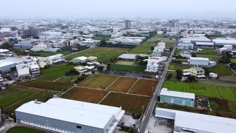 A-diverse-urban-landscape-transitioning-into-farmland,-on-a-cloudy-day,-aerial-view