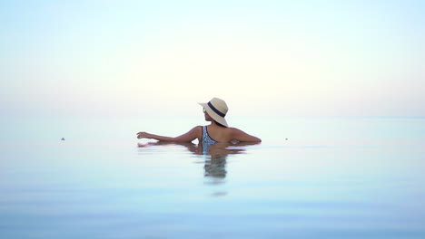 lonely female with hat in infinity pool looking at skyline