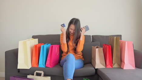 young asian woman using phone buying online shopping by credit card, feeling happy