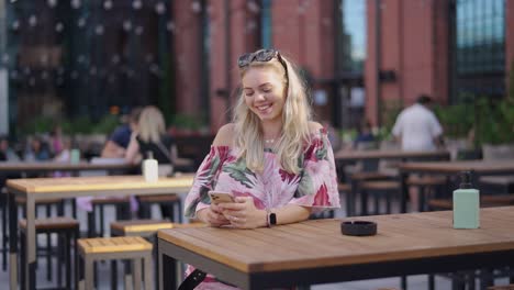 woman smiling at smartphone in outdoor cafe