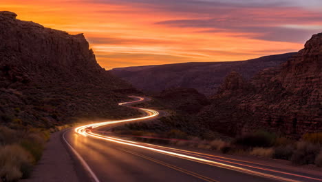 winding desert road with car light trails at sunset