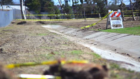 An-empty-desolate-park-enclosed-by-a-chain-link-fence-where-the-wind-blows-caution-tape-attached-to-a-construction-barrier-just-off-a-cement-path