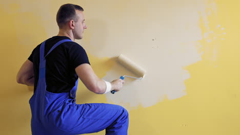 painter man with a roller brush. builder at work painting wall. makeover and renovation indoors. professional painting services.