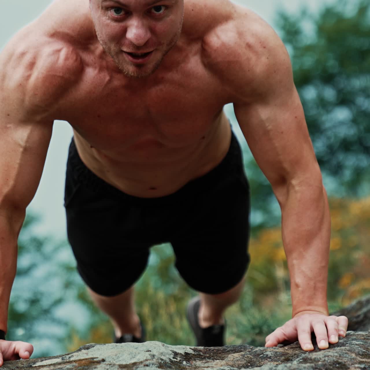 Front view of a strong man standing in plank. Athlete doing pushups on the rock. Blurred nature backdrop