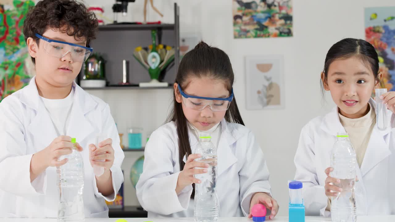 Tre asiatiske studerende i laboratoriekitler udfører et fysikeksperiment ved hjælp af vandflasker og bolde.